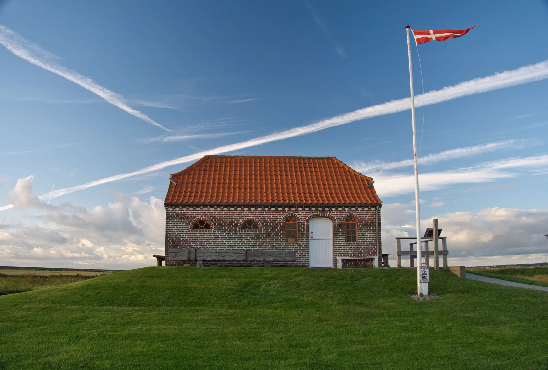 Dansk murstenshus med rødt tegltag på en nyslået græsflade, med Dannebrog på hvid flagstang